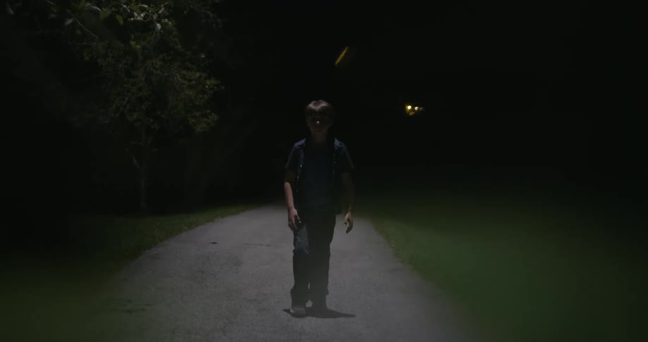 A boy is walking alone on a dirt road at night