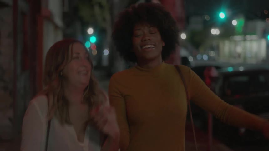 Two women walk down a city sidewalk at night