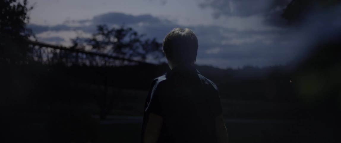 A boy is walking toward a railroad bridge at dusk