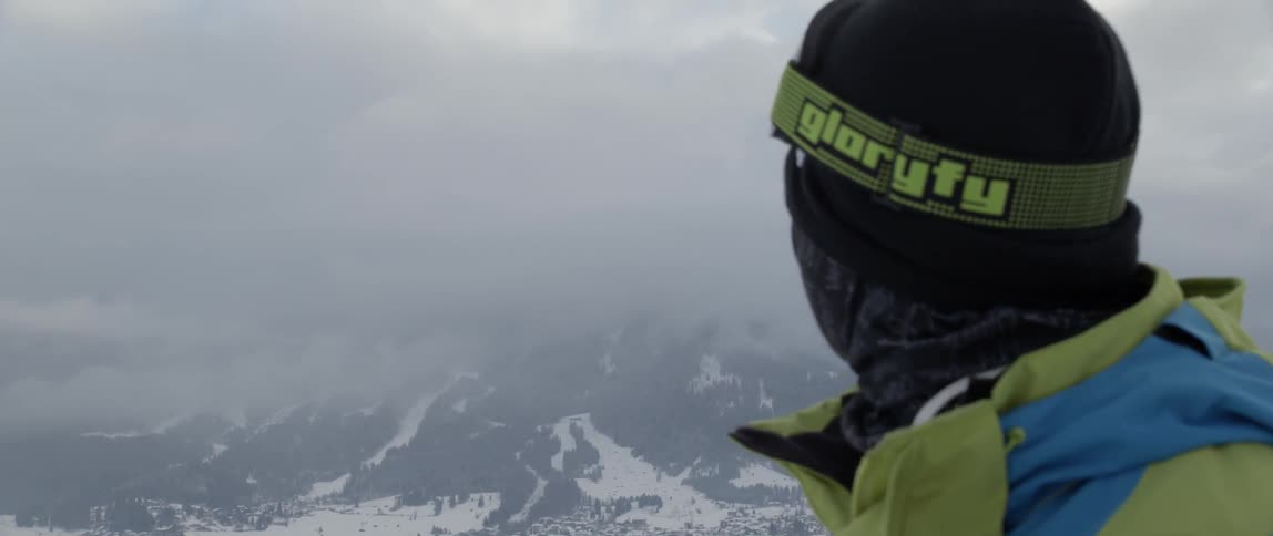 A man in snowboarding gear turns to look at a mountain