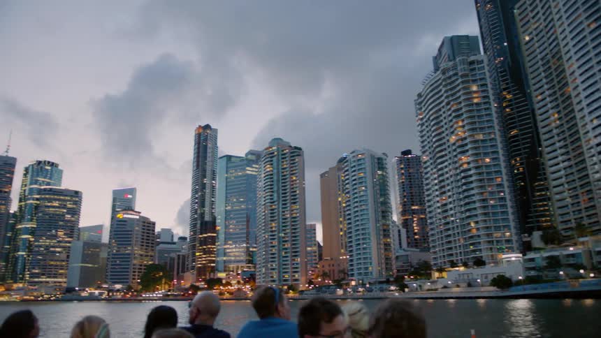 Tourists on a boat take pictures of a city at dusk