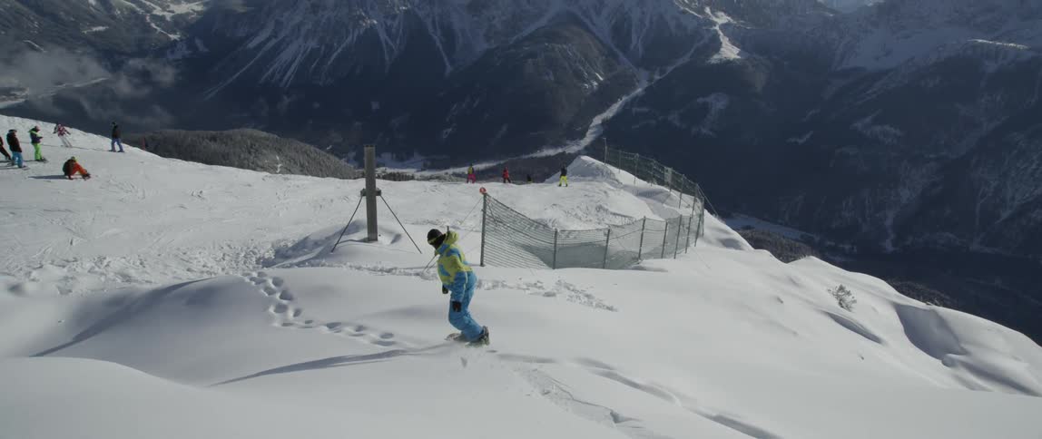 A snowboarder rides down a slope towards a group of people