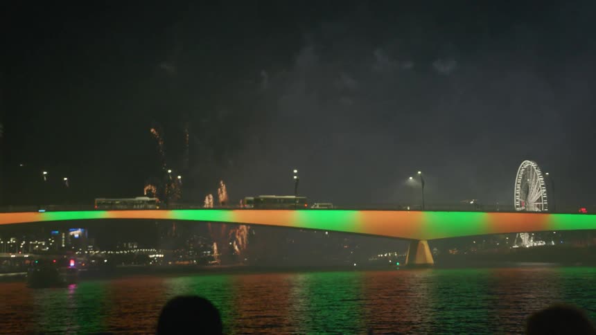 People are watching a fireworks display at night from a boat on a river