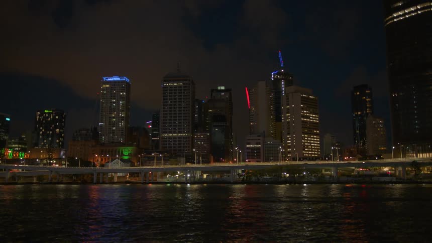 Tall city buildings illuminate the night sky above a bridge