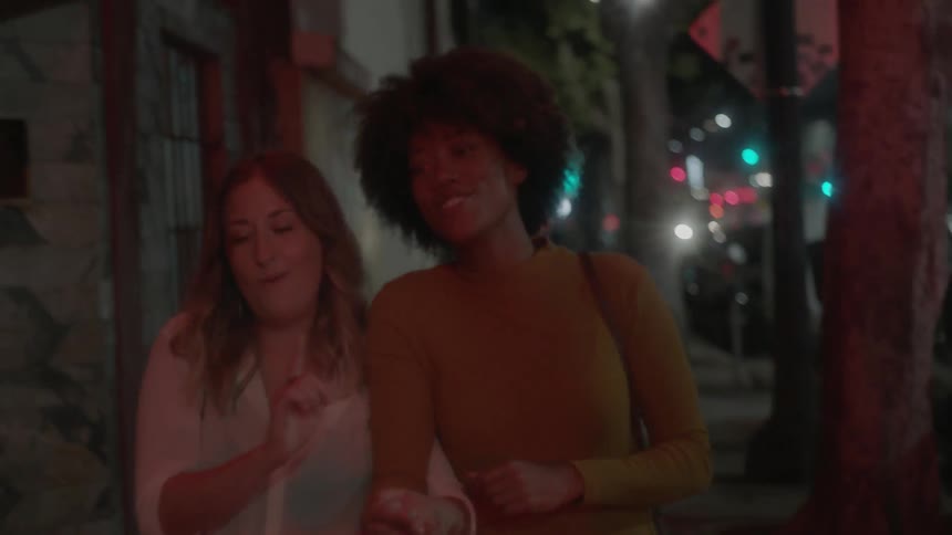 Two women walk down a city sidewalk at night