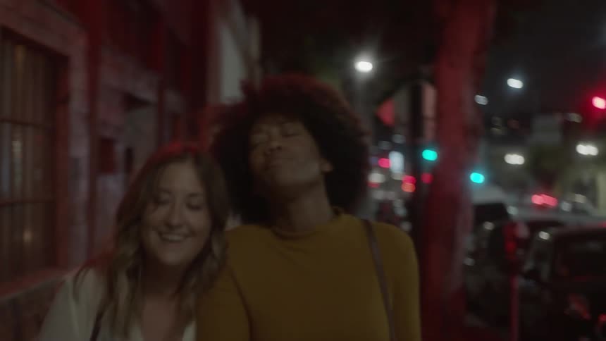 Two women laugh and walk down a city street at night