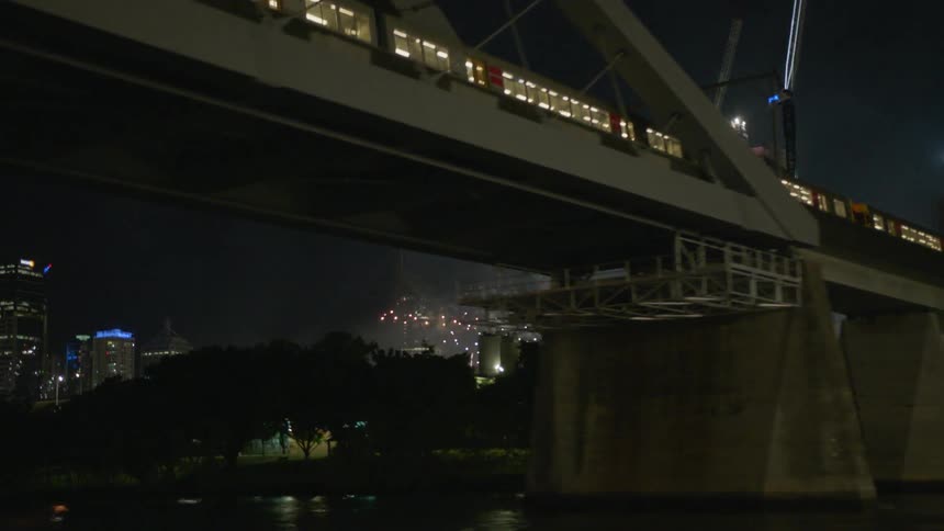 Fireworks light up the sky as a train crosses a bridge at night