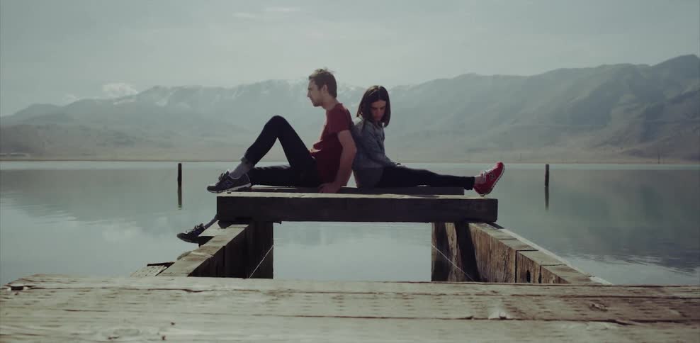 A couple sit back to back on a dock