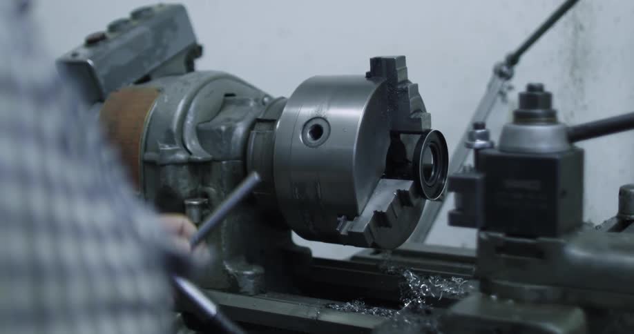 A large metal piece of a machine spinning and a man placing something in a hole in it