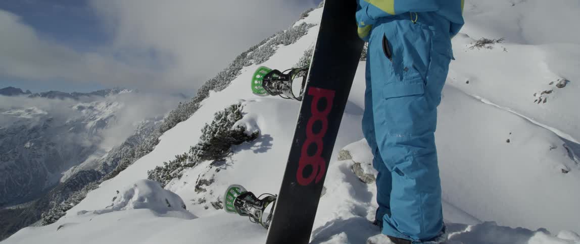 A man with a snowboard stands on a mountain peak taking in the view