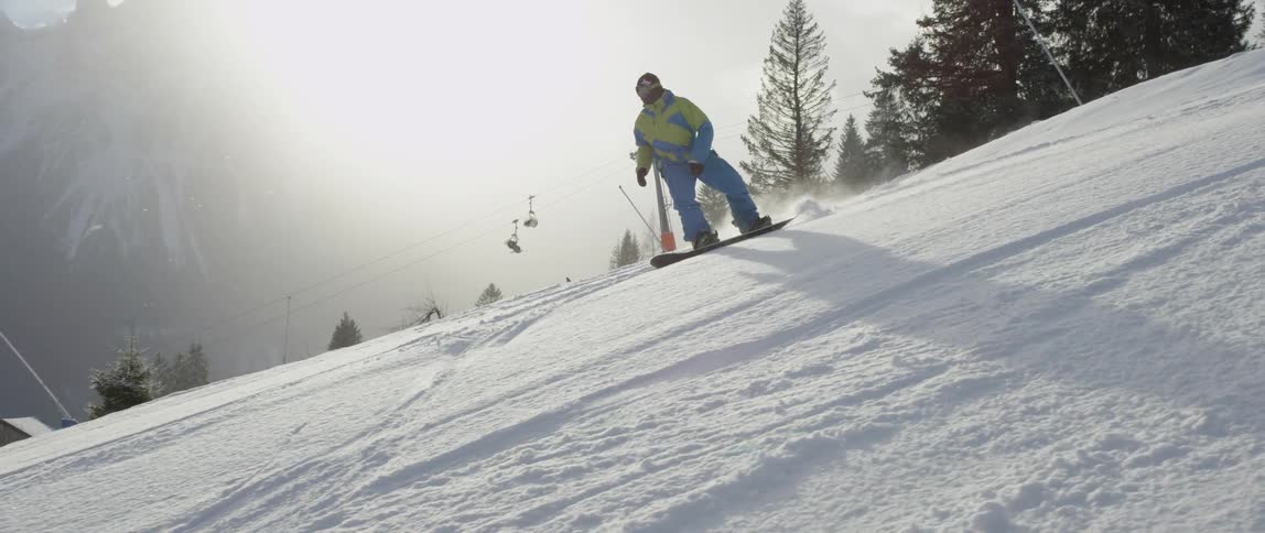A snowboarder rides down a mountain in a ski resort during the day