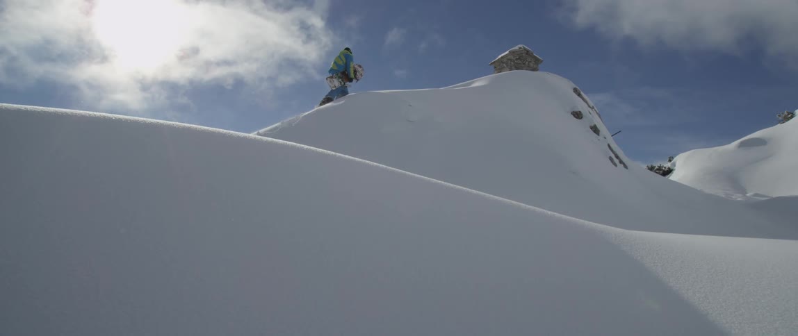 Person carrying snowboard walks up a snowy peak