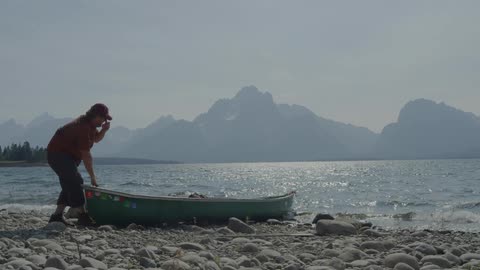 A man pulls a canoe ashore at a lake during the day