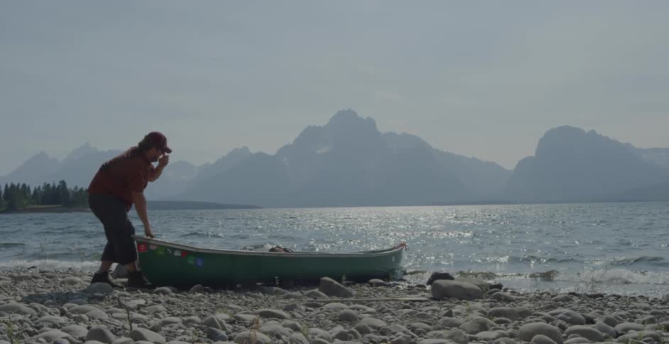 A man pulls a canoe ashore at a lake during the day