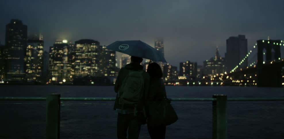 Couple stands looking at a river and city at night