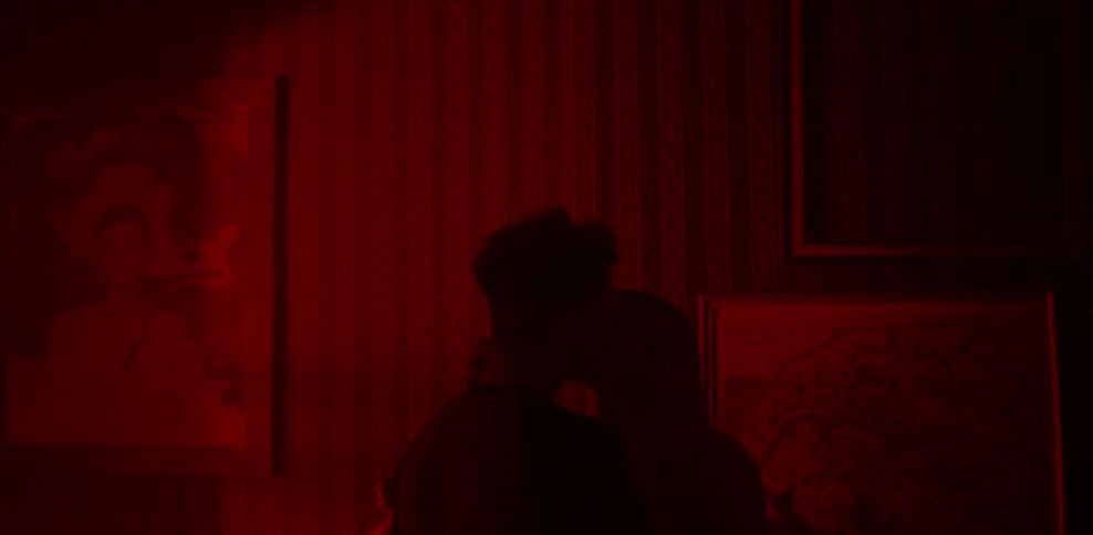 A man and woman kiss in a dimly lit room