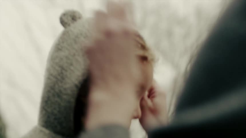 A mother pulls up the hood on her daughter's jacket on a snowy day