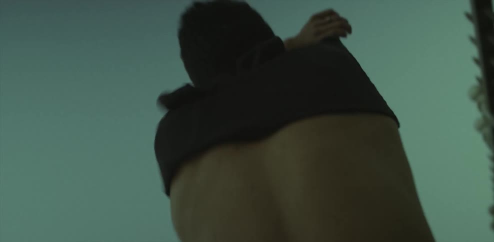 A man takes off his shirt as he is walking at dusk