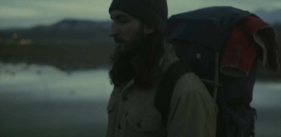 A man carrying a heavy backpack is hiking in a natural setting at dusk