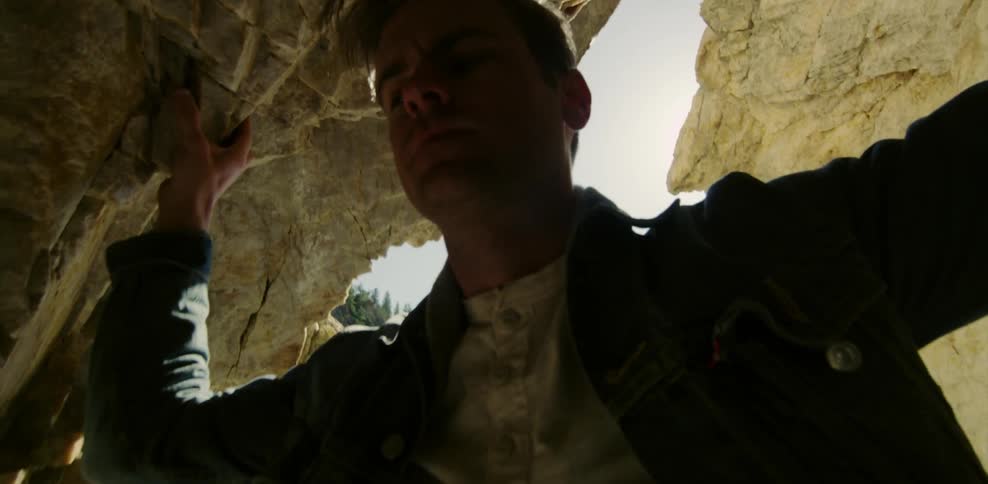A man looking inside a cave with the sun in the back