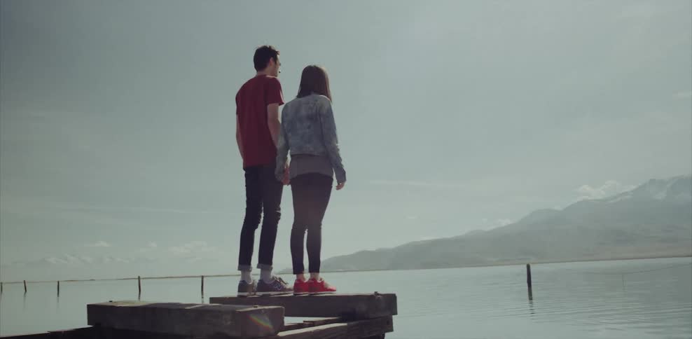 A man and woman are standing on the end of a pier holding hands