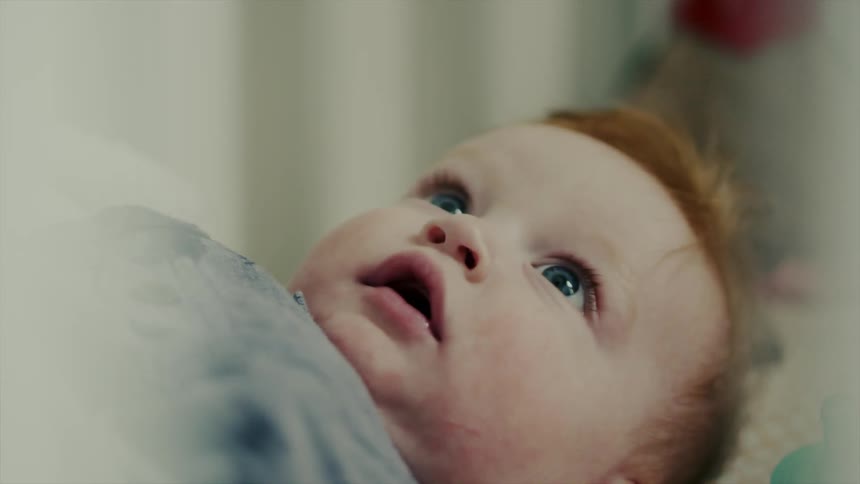 A baby looks upwards as it lies in bed during the day