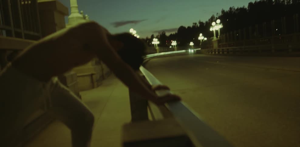 Shirtless man leans on a guardrail next to a busy road