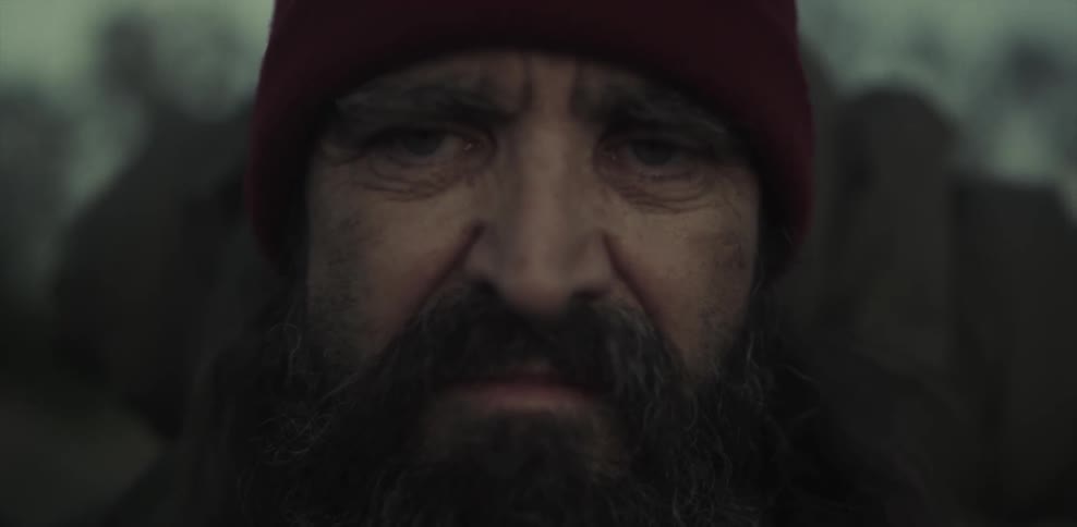 A dirty, bearded man blinks tiredly