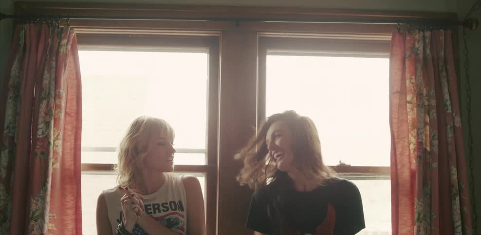 Two women laugh and talk while sitting in front of window during the day