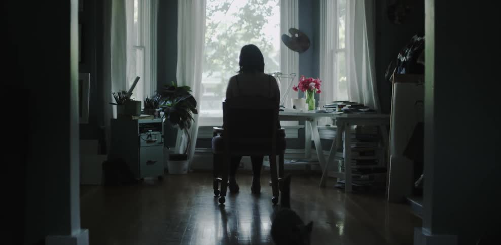 A cat rubs against a chair where a woman sits