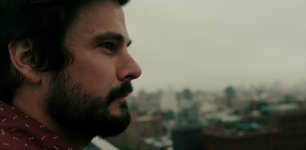 Man leaning over balcony railing looking at a city