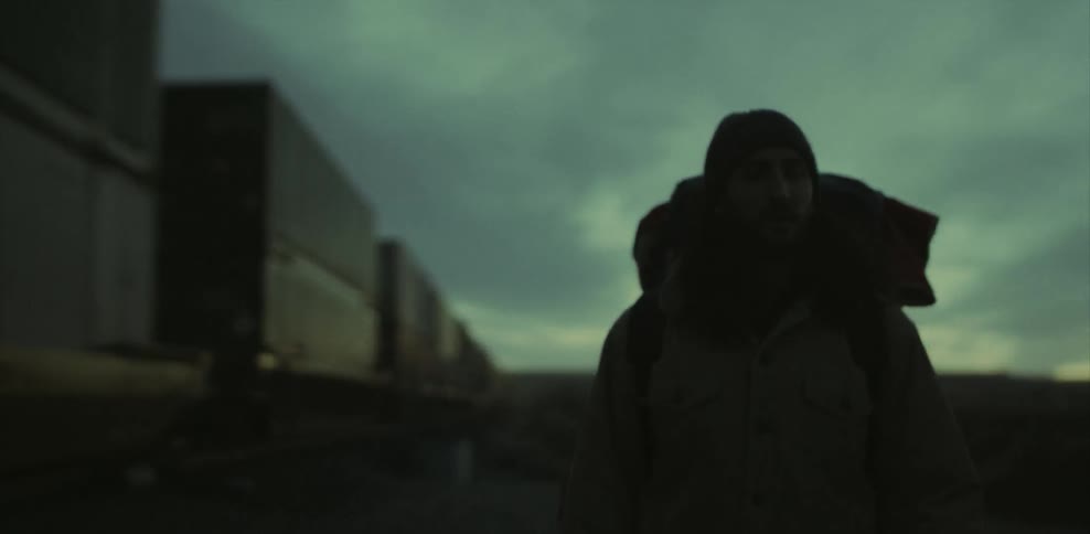 A man carrying a heavy backpack is hiking near a passing train at dusk