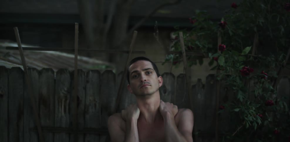 A man sitting outside near a fence nods and runs his hands over his head