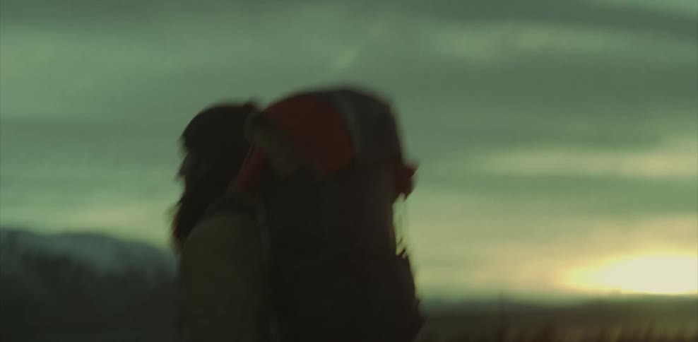 A man hikes with a backpack near mountains at sunset