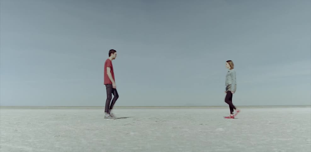 A man and woman walk up to each other on a salt flat