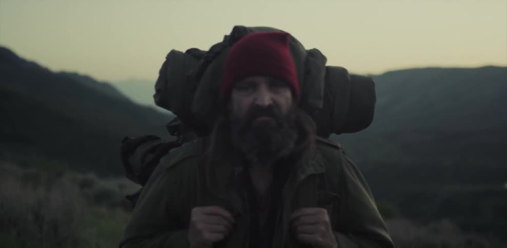 A man stands in the mountains with a backpack at sunset