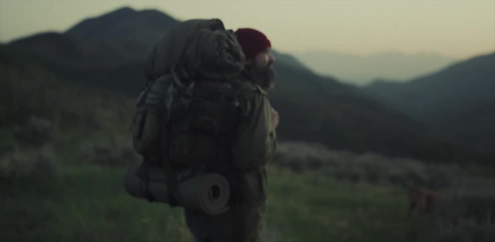 A man carrying a heavy backpack is stopped looking at the scenery