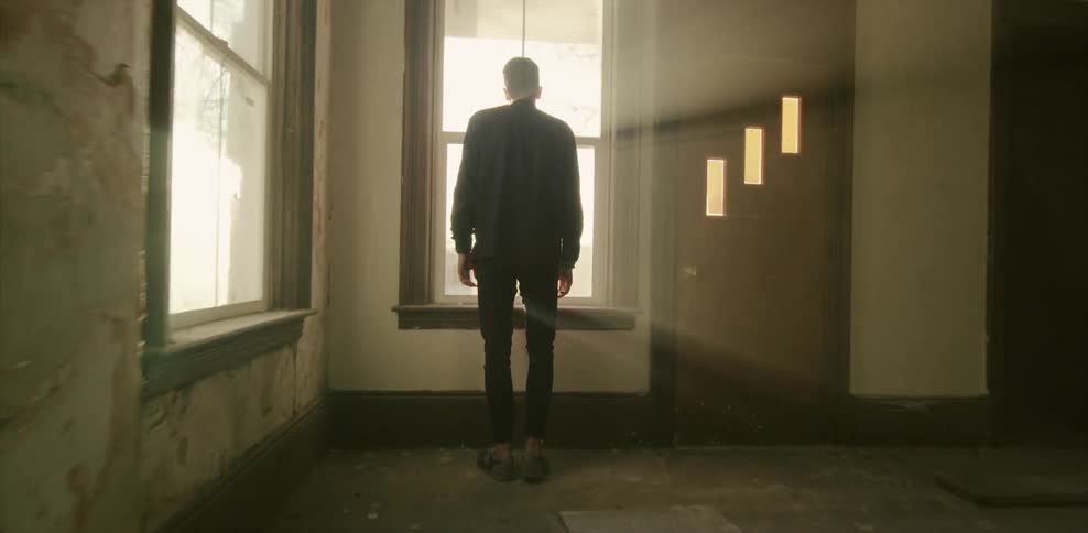 Man standing in an empty room looking out a window on a sunny day