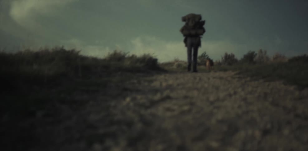A man wearing a large backpack walks up a dirt path