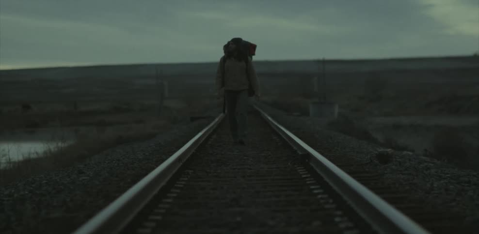 Man wearing a backpack walks down railroad tracks