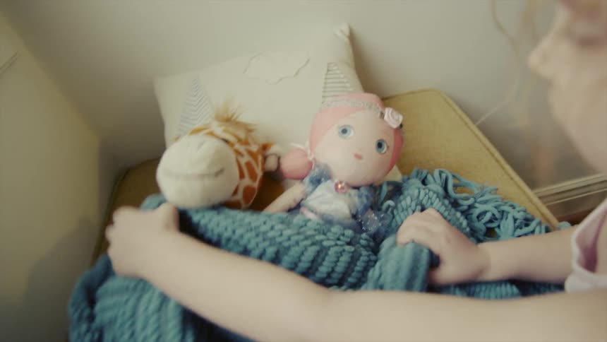 Child putting a stuffed animal in bed and covering it up