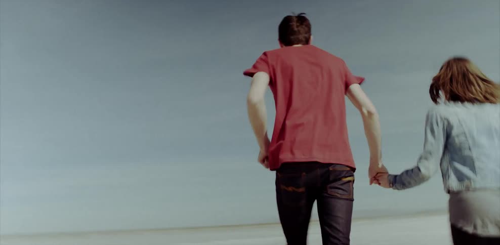 A man and woman run through the desert holding hands