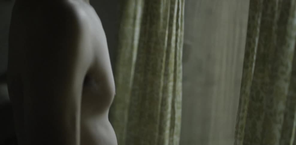 Shirtless man looking out a window as traffic passes by