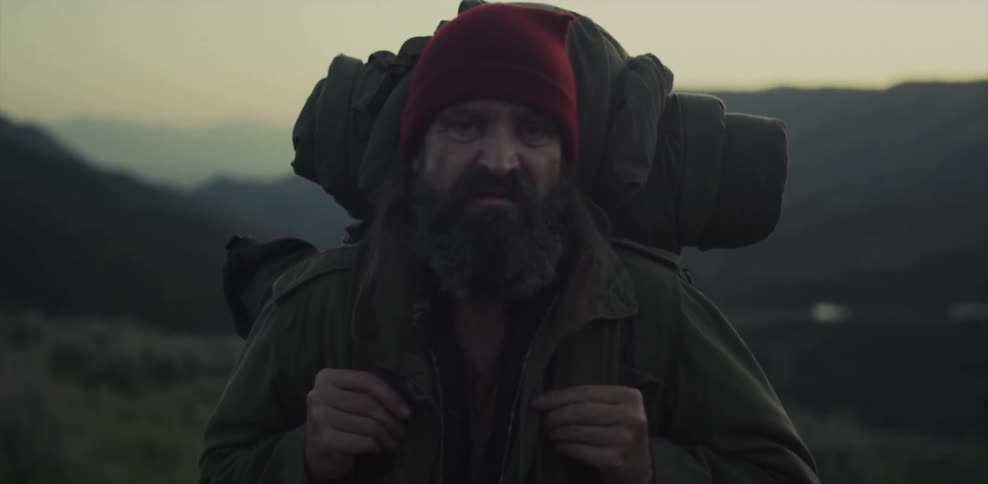 A bearded man stands with a backpack