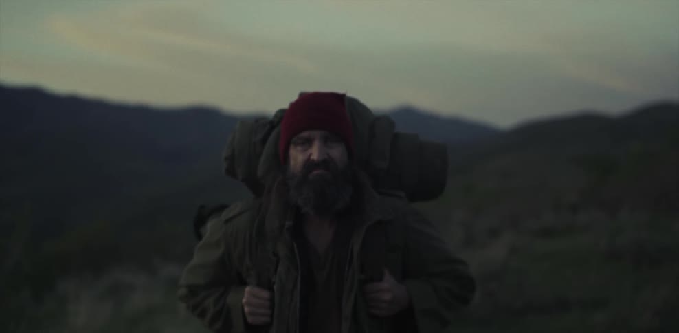 A man is standing still and gripping his backpack straps in a hilly area