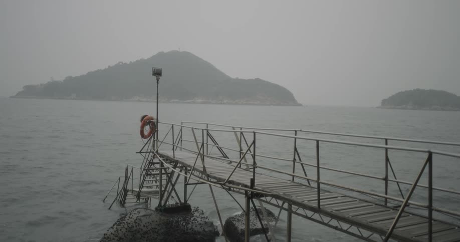 Waves lap rocks and the pilings of a narrow pier