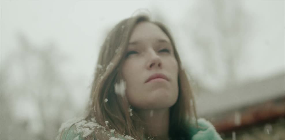 A woman standing outside looking up as the snow falls