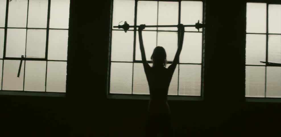 A man standing in front of a window holds a barbell over his head
