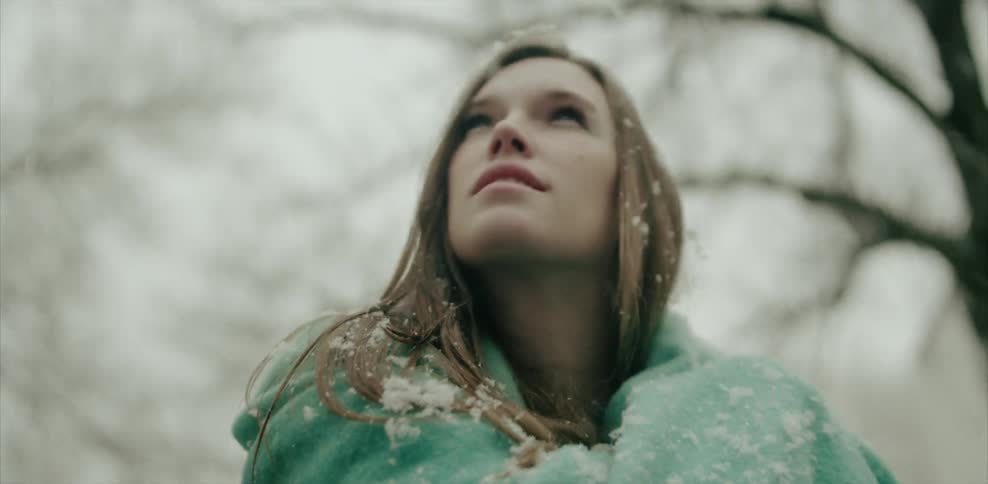 Snow falls on a woman as she walks beneath trees