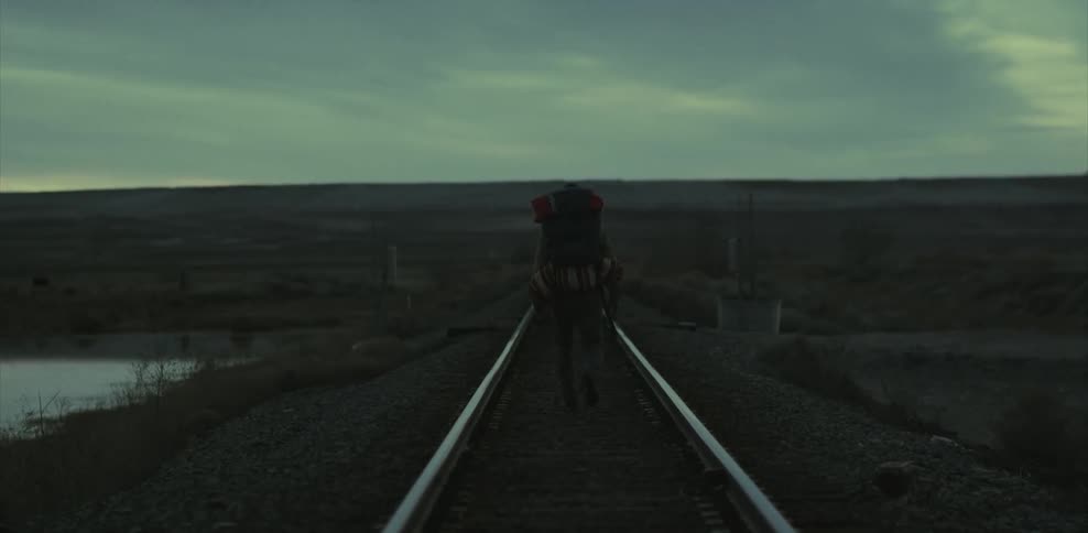 Man walks down middle of railroad tracks with large backpack
